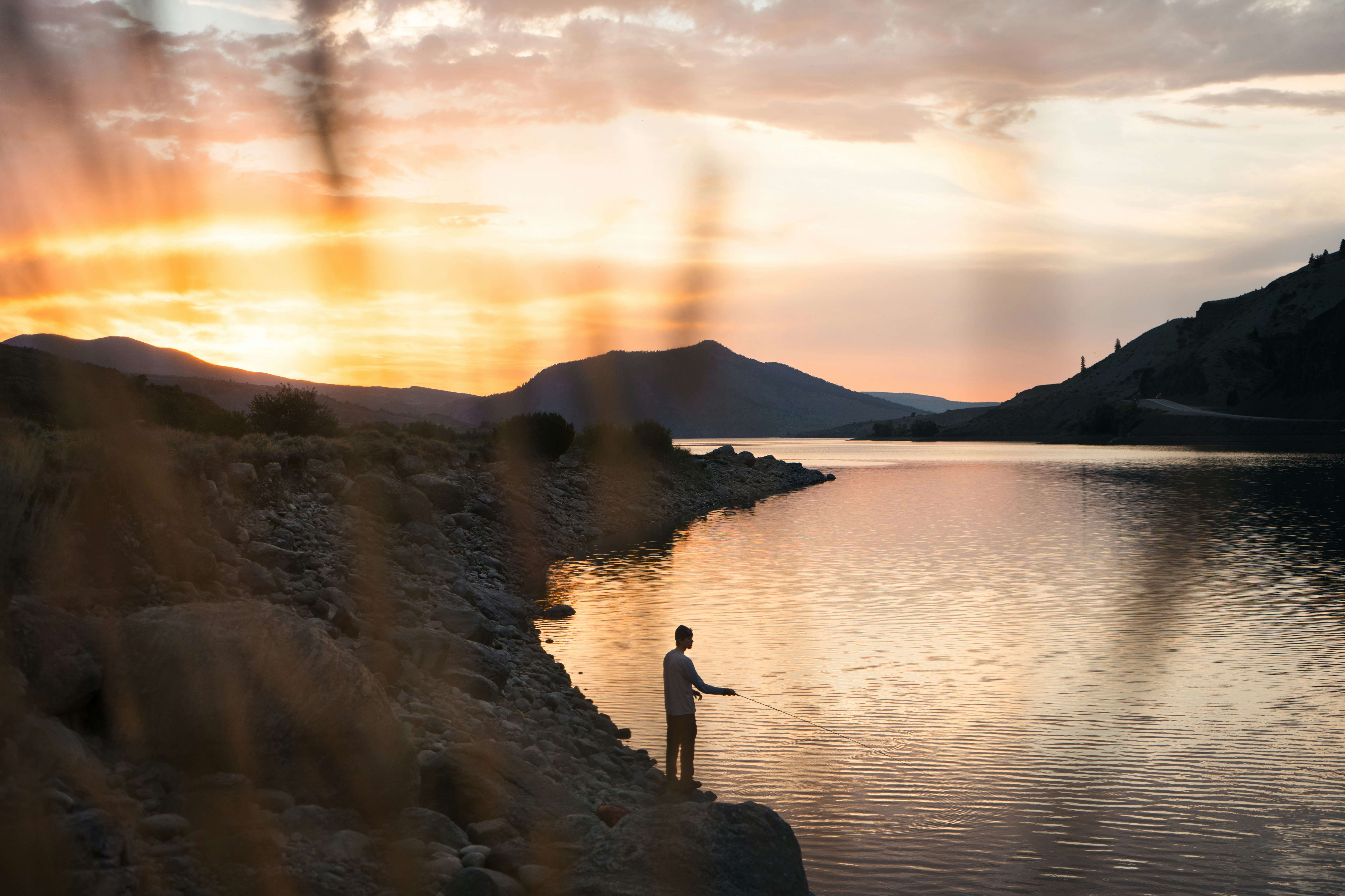 person standing on rock near body of water during sunset